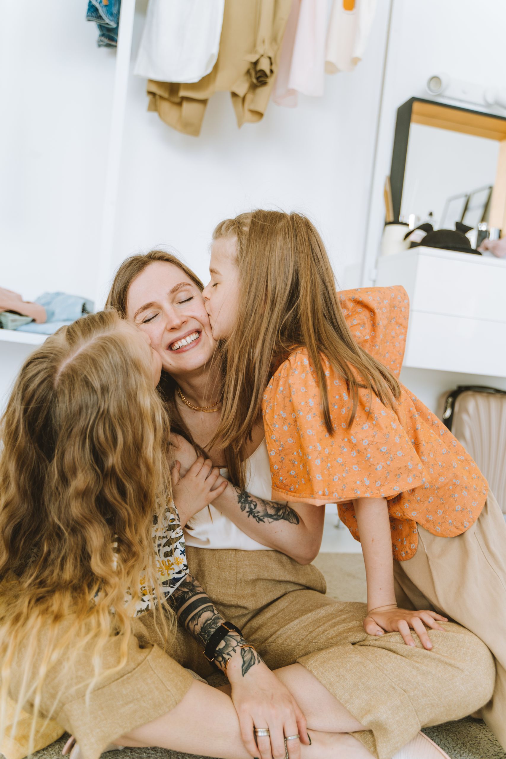 A joyful mother receives affectionate kisses from her two daughters in a cozy indoor setting.