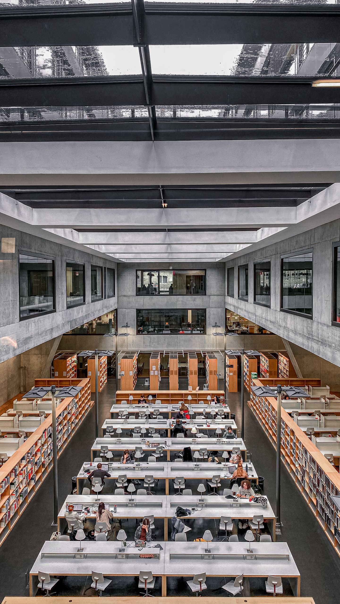 High-angle view of a modern university library interior with students studying under a skylight.